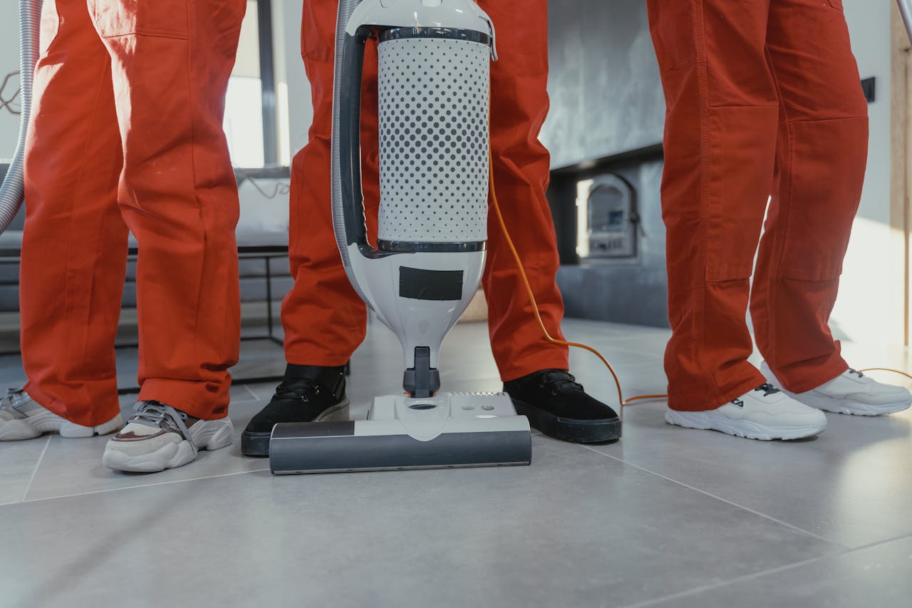home-services-004 Team of professional cleaners in red uniforms using a vacuum cleaner indoors.