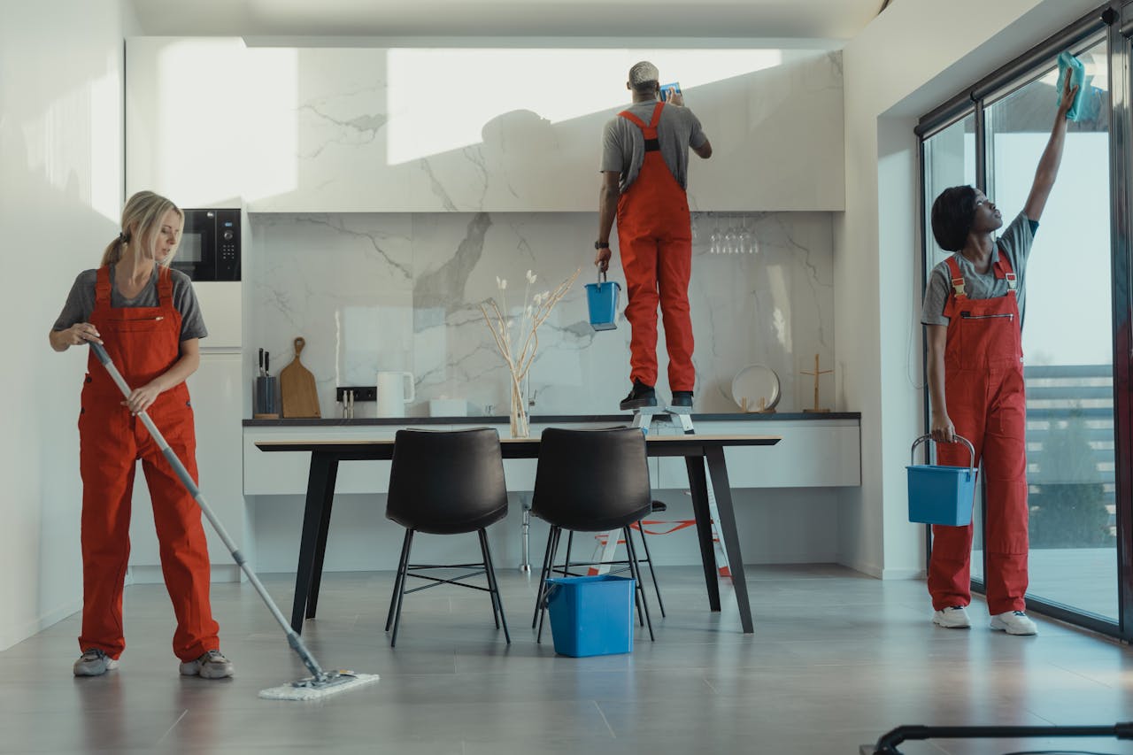 cta-bg Group of cleaners in red uniforms mopping and wiping glass in a modern dining room.