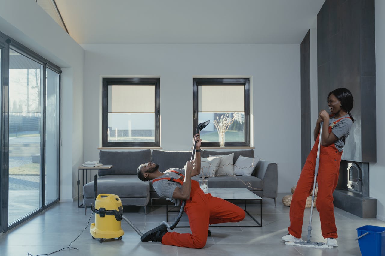 home-services-03 Fun and engaging cleaning session with a man and woman in overalls using cleaning tools in a modern living room.